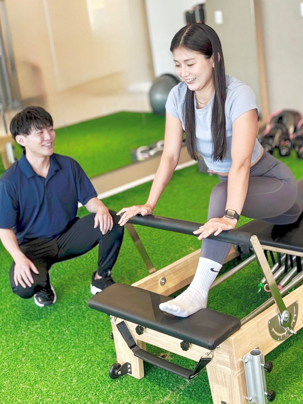 トレーナーのサポートを受けながらマシンピラティスを体験する女性